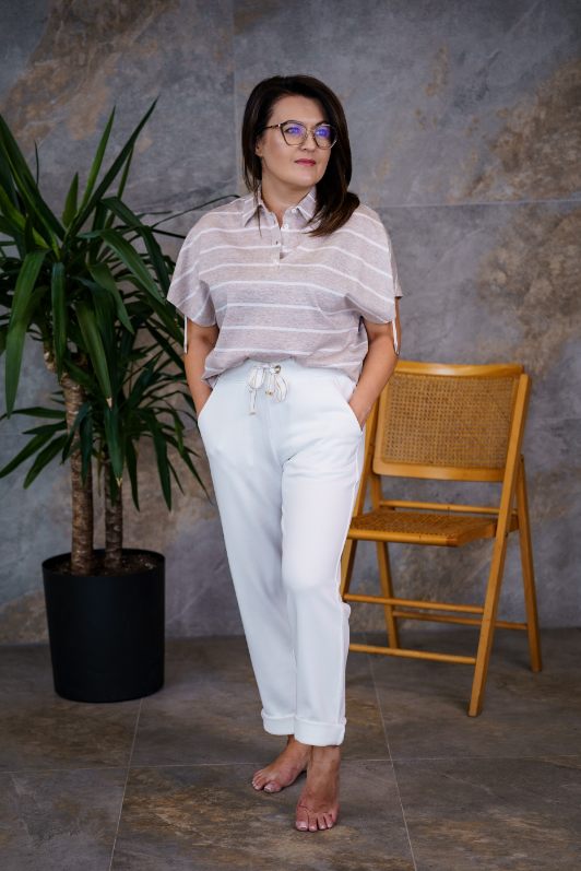 image000001 Beżowo-biała bluzka polo w paski o swobodnym, nowoczesnym kroju. Model z klasycznym kołnierzykiem i krótkim zapięciem na guziki. Szerokie, opadające rękawy bez wyraźnie zaznaczonej linii ramion nadają sylwetce lekkości i komfortu. Ozdobne troczki po bokach rękawów stanowią subtelny detal podkreślający minimalistyczny charakter projektu. Poziome paski w odcieniach beżu i bieli dodają całości świeżego, letniego wyglądu. Idealna do codziennych stylizacji – doskonale komponuje się z białymi spodniami, lnianymi szortami lub spódnicą, tworząc elegancki, a zarazem niezobowiązujący outfit.