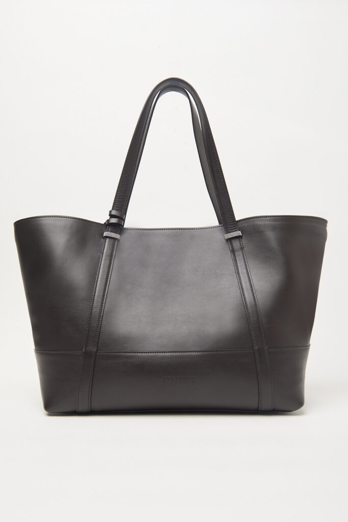 A38389C0R CC878 953 2 Elegancka torba shopper Peserico to doskonałe połączenie funkcjonalności i ponadczasowego włoskiego designu. Wykonana z wysokiej jakości naturalnej skóry w modnym czekoladowym odcieniu, zachwyca minimalistycznym stylem oraz starannym wykończeniem charakterystycznym dla marki Peserico. Przestronne wnętrze sprawia, że torba doskonale sprawdzi się zarówno na co dzień, do pracy, jak i podczas podróży czy zakupów. Model wyposażono w wygodne, długie uchwyty do noszenia na ramieniu oraz odpinany, regulowany pasek, który umożliwia noszenie torby również crossbody lub na ramieniu, zapewniając maksymalny komfort użytkowania. Subtelne logo marki oraz charakterystyczne metaliczne detale dodają całości luksusowego charakteru, czyniąc torbę uniwersalnym dodatkiem do eleganckich i codziennych stylizacji.