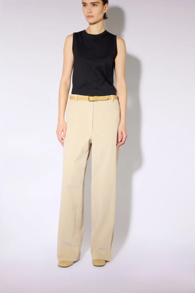 W6LL6WO21W45 1 B PANTALONE COLBY Spodnie sztruksowe damskie w eleganckim, kremowym odcieniu to ponadczasowy model łączący wygodę z nowoczesnym stylem. Wykonane z miękkiego sztruksu, wyróżniają się charakterystyczną prążkowaną fakturą, która nadaje stylizacji wyrazistego, szlachetnego charakteru. Model ma prosty, szeroki fason z długimi nogawkami, średni stan oraz klasyczne zapięcie w pasie. Jasny, neutralny kolor doskonale komponuje się zarówno z czernią i brązami, jak i z pastelowymi odcieniami. Spodnie sztruksowe świetnie sprawdzą się w stylizacjach casualowych, biurowych oraz bardziej eleganckich.